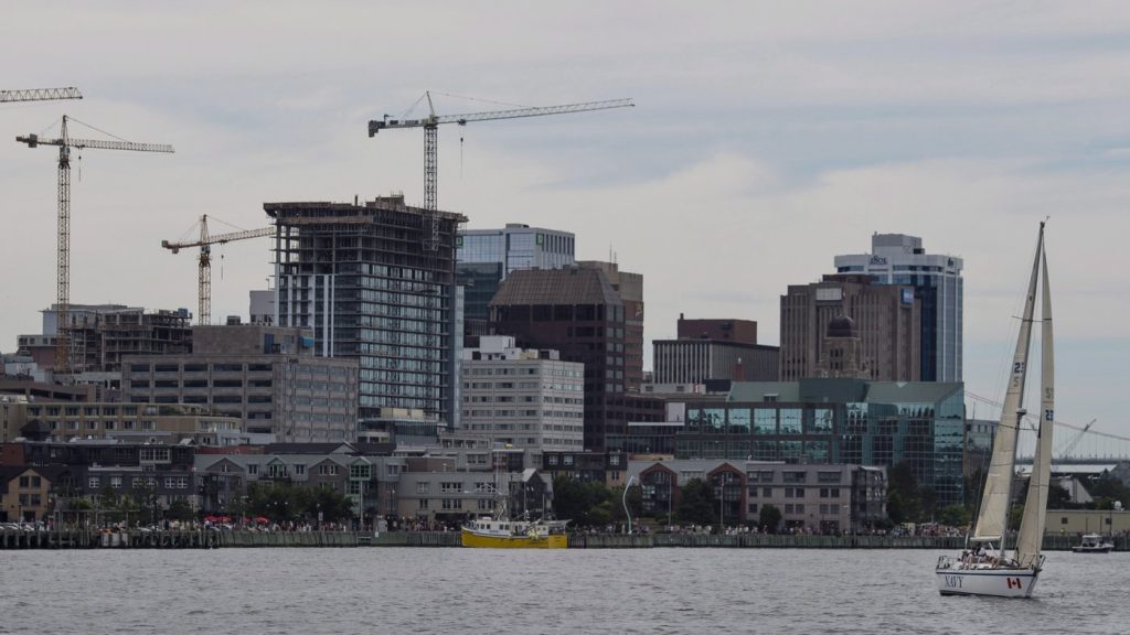 A sailboat is seen in front of the Halifax skyline as construction cranes work in the