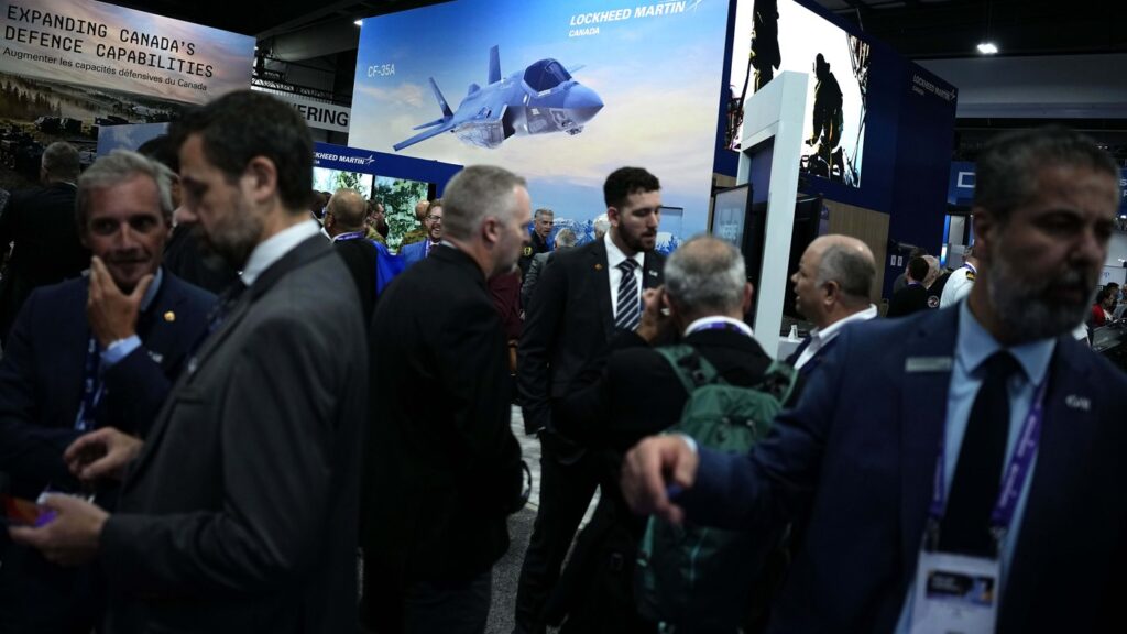 People walk the exhibition floor below a photo of a Lockheed Martin F-35 multirole combat aircraft, at the Canadian Association of Defence and Security Industries annual defence industry trade show CANSEC, in Ottawa, on Wednesday, May 27, 2026. THE CANADIAN PRESS/Justin Tang